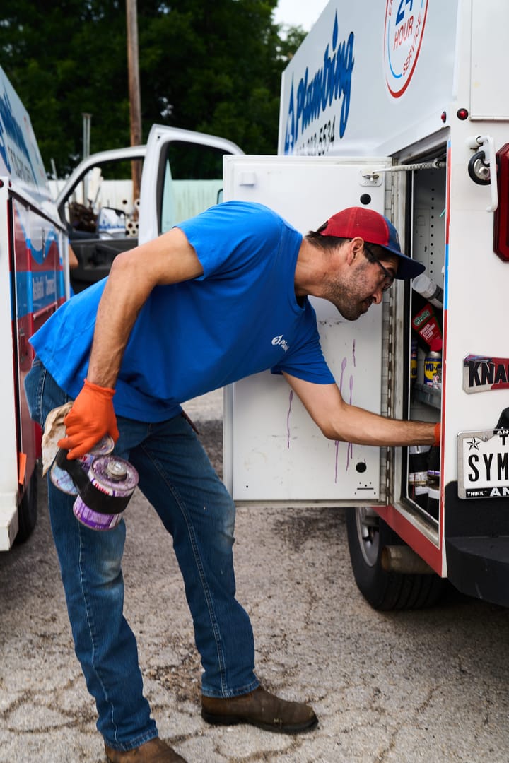 Plumber in a blue shirt and red cap accessing tools in a work van.
