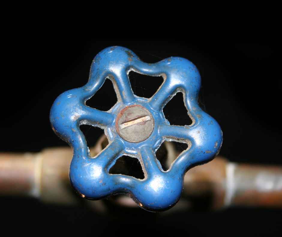 Blue metal valve wheel on a pipe, likely a water shut-off valve against a dark background.